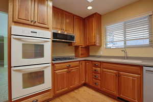 Kitchen featuring stainless steel appliances, brown cabinetry, light wood-style flooring, recessed lighting, and light stone counters