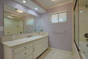 Bathroom featuring crown molding, combined bath / shower with glass door, vanity, light tile patterned floors, and healthy amount of natural light