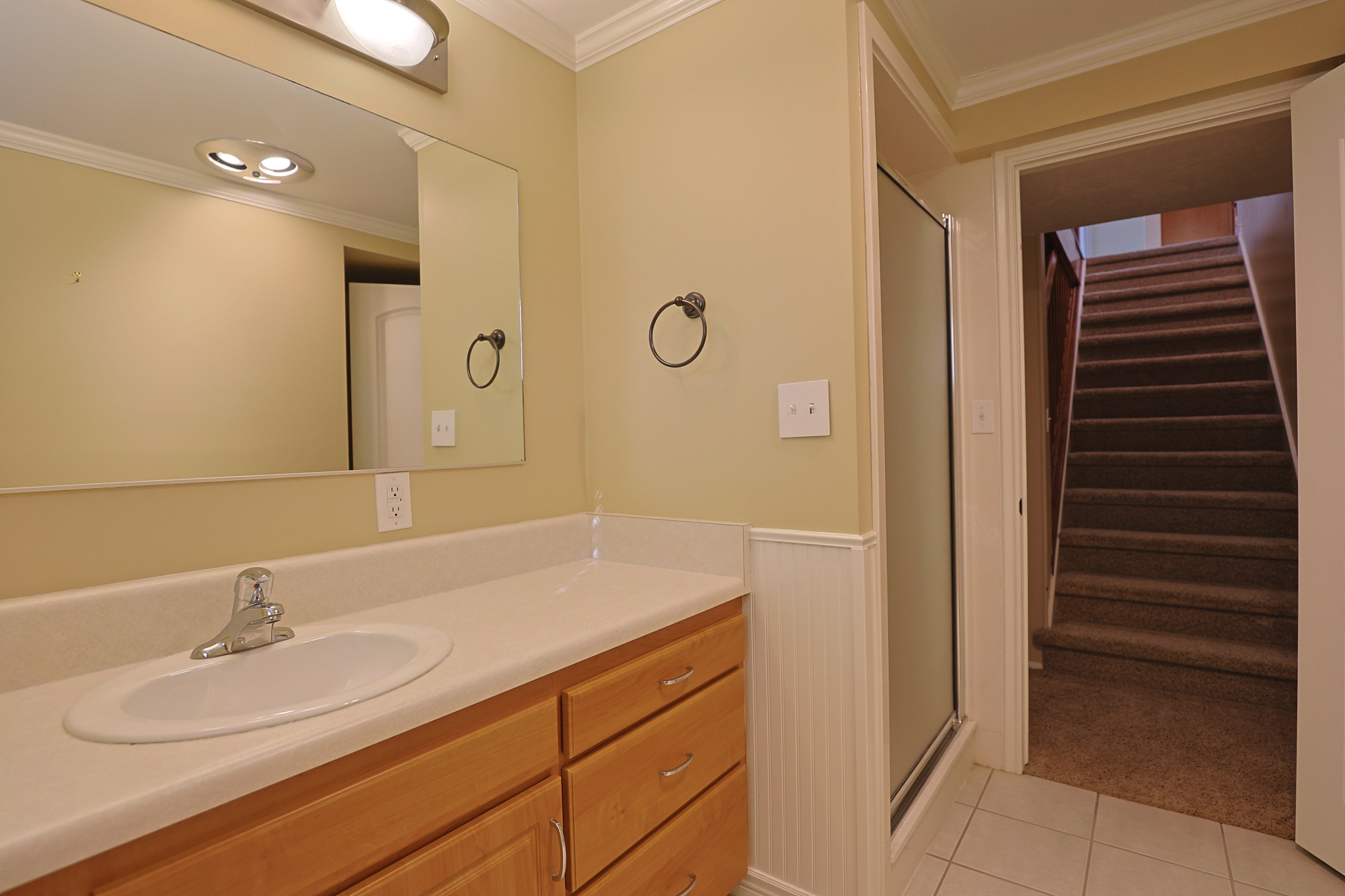 Bathroom featuring crown molding, vanity, light tile patterned floors, a stall shower, and wainscoting