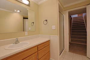 Bathroom featuring crown molding, vanity, light tile patterned floors, a stall shower, and wainscoting
