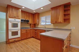 Kitchen with open shelves, white double oven, a skylight, recessed lighting, and brown cabinets