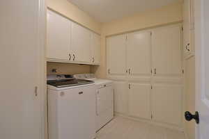 Washroom featuring cabinet space, light tile patterned floors, and independent washer and dryer