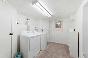 Laundry area featuring light colored carpet, washing machine and dryer, and a textured ceiling