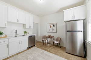 Kitchen featuring stainless steel appliances, white cabinets, wood tiled floors, and light stone counters