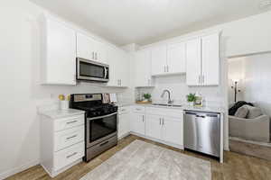 Kitchen with stainless steel appliances, white cabinetry, light stone counters, and wood tiled floors