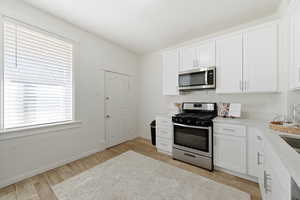 Kitchen featuring stainless steel appliances, white cabinets, wood finish floors, and light stone countertops