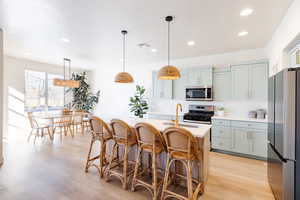 Kitchen featuring a kitchen bar, stainless steel appliances, pendant lighting, gray cabinets, and a kitchen island with sink