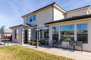 Rear view of property featuring a trampoline, a patio, stucco siding, a lawn, and outdoor dining space