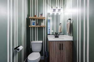 Half bath featuring wallpapered walls and vanity