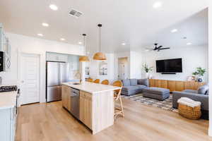 Kitchen featuring a breakfast bar area, hanging light fixtures, stainless steel appliances, and open floor plan