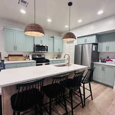 Kitchen with stainless steel appliances, pendant lighting, light wood-style floors, a breakfast bar area, and recessed lighting