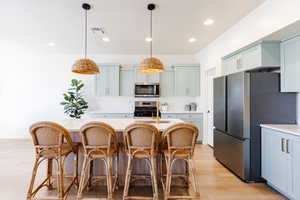 Kitchen featuring a breakfast bar area, light wood-type flooring, stainless steel appliances, a kitchen island with sink, and gray cabinets