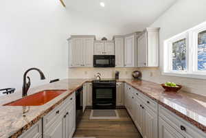Kitchen featuring vaulted ceiling, black appliances, light stone counters, dark wood-style floors, and decorative backsplash