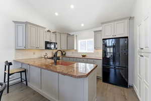 Kitchen featuring a peninsula, black appliances, lofted ceiling, light stone countertops, and a kitchen bar