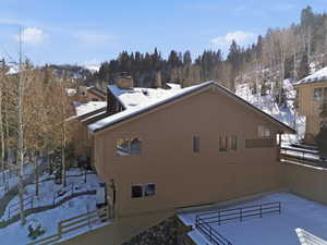 View of snow covered exterior featuring a chimney and a forest view