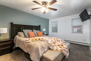 Bedroom with carpet, baseboard heating, a textured ceiling, and a ceiling fan