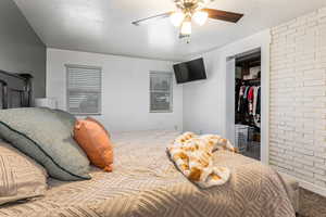 Bedroom featuring a textured ceiling, carpet flooring, a walk in closet, ceiling fan, and brick wall