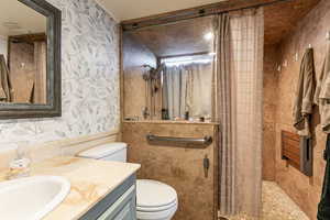 Full bathroom with wainscoting, wallpapered walls, tiled shower, and vanity