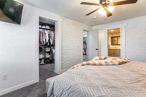 Bedroom featuring brick wall, a textured ceiling, dark colored carpet, a spacious closet, and ensuite bath