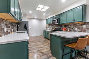 Kitchen with green cabinetry, light stone countertops, a kitchen bar, appliances with stainless steel finishes, and a peninsula