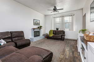 Living room with a textured ceiling, a premium fireplace, dark wood-type flooring, and ceiling fan