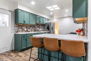 Kitchen with a kitchen bar, green cabinetry, a peninsula, backsplash, and stainless steel fridge