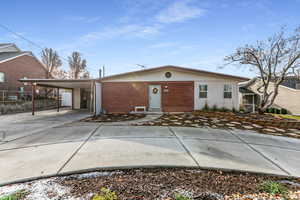 View of front facade with driveway, brick siding, a carport, and a patio
