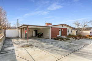Back of property with concrete driveway, brick siding, a chimney, and a carport