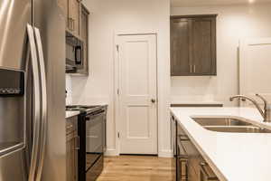 Kitchen with black appliances, light wood-type flooring, dark brown cabinets, and light stone countertops