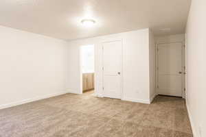 Unfurnished bedroom featuring a textured ceiling, light carpet, ensuite bath, and a closet
