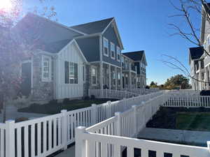 View of side of home with board and batten siding, a fenced backyard, stone siding, roof with shingles, and a porch