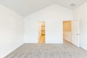 Primary bedroom with light colored carpet and high vaulted ceiling