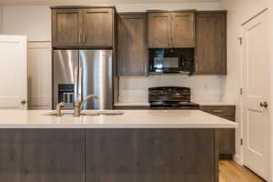 Kitchen featuring dark brown cabinets, black appliances, light stone counters, and light wood finished floors