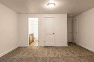 Unfurnished bedroom featuring a textured ceiling, light colored carpet, connected bathroom, and a closet