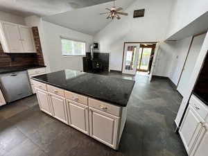 Kitchen featuring a wood stove, a kitchen island, dishwasher, ceiling fan, and dark stone counters