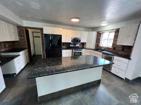 Kitchen featuring stainless steel appliances, a center island, white cabinetry, and a textured ceiling