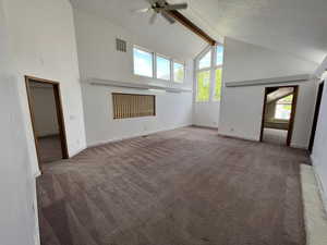 Unfurnished living room featuring high vaulted ceiling, beam ceiling, carpet floors, ceiling fan, and a textured ceiling