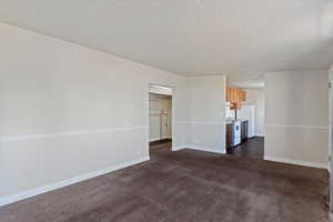 Unfurnished living room featuring a textured ceiling and dark colored carpet