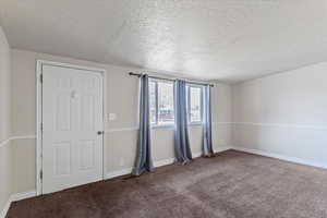 Carpeted spare room featuring a textured ceiling and baseboards
