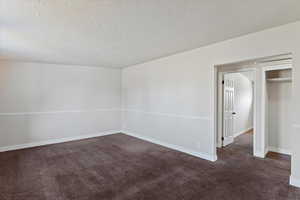 Unfurnished room featuring a textured ceiling and dark carpet