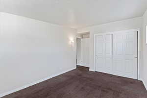 Unfurnished bedroom featuring dark colored carpet, a closet, and a textured ceiling