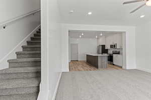 Kitchen featuring open floor plan, a center island with sink, light countertops, stainless steel appliances, and a ceiling fan
