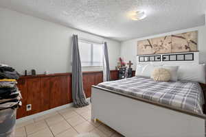 Bedroom featuring a textured ceiling, wainscoting, wooden walls, and light tile patterned floors