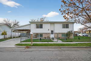 Raised ranch featuring brick siding, concrete driveway, a fenced front yard, a carport, and a gate