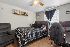 Bedroom with wood finished floors, a ceiling fan, and a desk