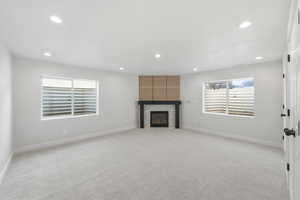Unfurnished living room with a large fireplace, light carpet, and recessed lighting