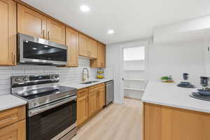 Kitchen featuring stainless steel appliances, light stone countertops, backsplash, light wood-style floors, and recessed lighting