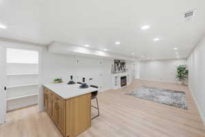 Kitchen featuring brown cabinetry, a glass covered fireplace, a kitchen bar, light wood-type flooring, and open floor plan