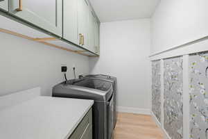 Washroom featuring light wood-type flooring, cabinet space, and separate washer and dryer