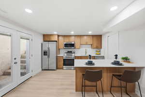 Kitchen featuring a breakfast bar, appliances with stainless steel finishes, a peninsula, decorative backsplash, and light wood-style floors